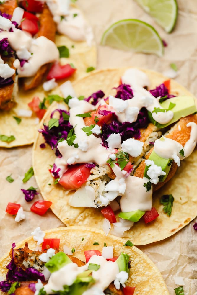 close up on a corn tortilla topped with vegan fish, purple cabbage, and white sauce on parchment paper