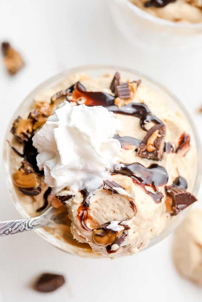 beige peanut butter mousse topped with chocolate sauce and whipped cream in a white bowl