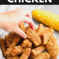 pinterest image of a womans hand taking a piece of fried vegan chicken from a pile on a white plate