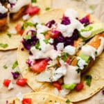 close up on a corn tortilla topped with vegan fish, purple cabbage, and white sauce on parchment paper