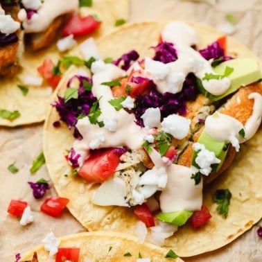 close up on a corn tortilla topped with vegan fish, purple cabbage, and white sauce on parchment paper