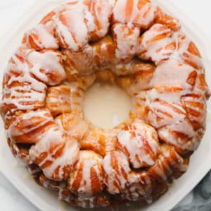 baked golden brown monkey bread on a white plate, covered in white icing