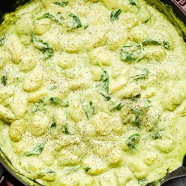 close up of large pot filled with a green cream sauce and gnocchi