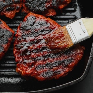 brushing red sauce on a charred vegan steak in a grill pan