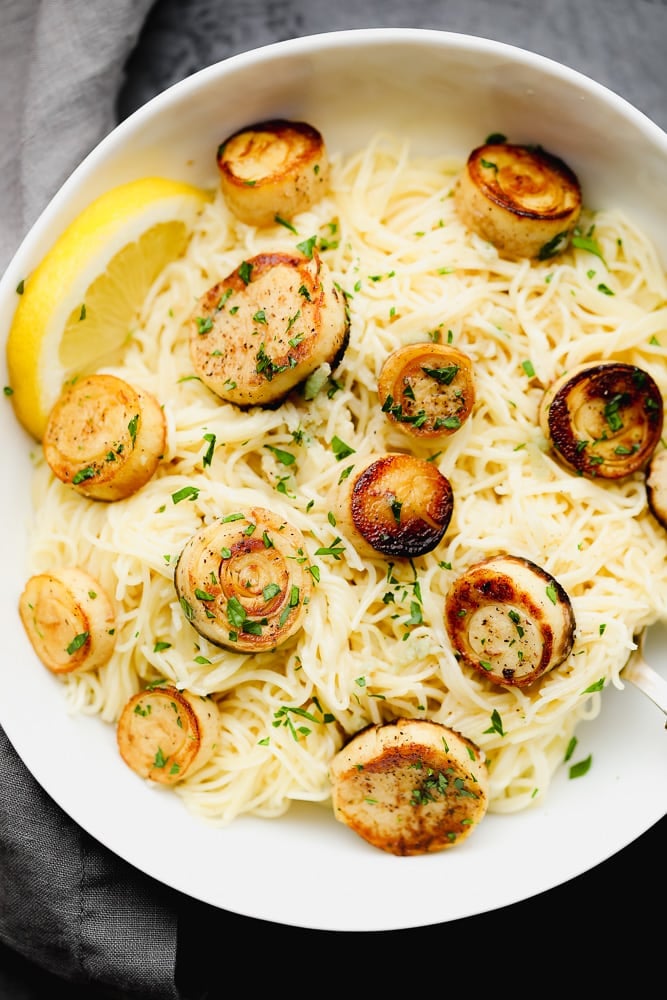 cooked pasta noodles topped with cooked vegan scallops in a white bowl