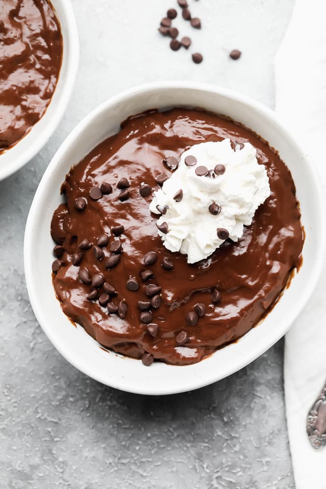 chocolate pudding in a white bowl topped with chocolate chips and whipped cream