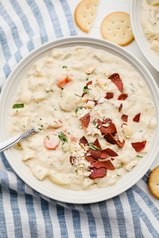 bowl of vegan clam chowder with vegan bacon on top, crackers around it