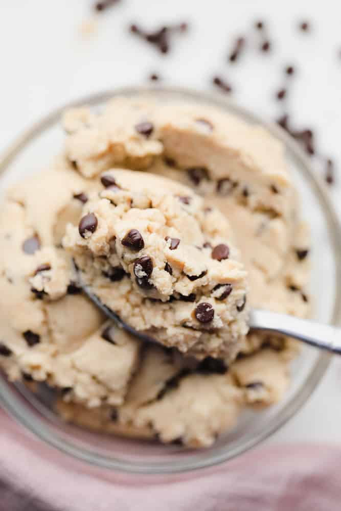 spoon taking a scoop of chocolate chip cookie dough out of a glass bowl