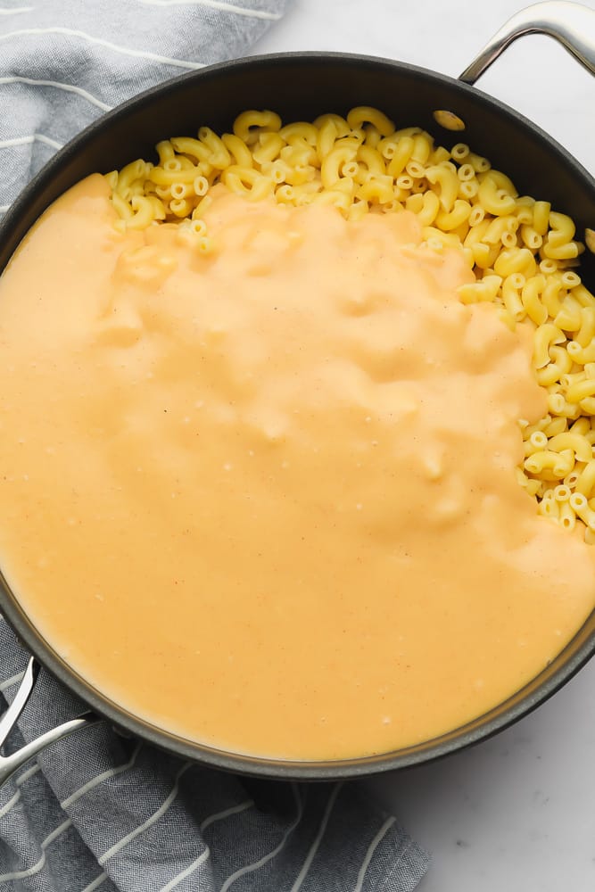 orange cheese sauce covering cooked macaroni in a large black skiller