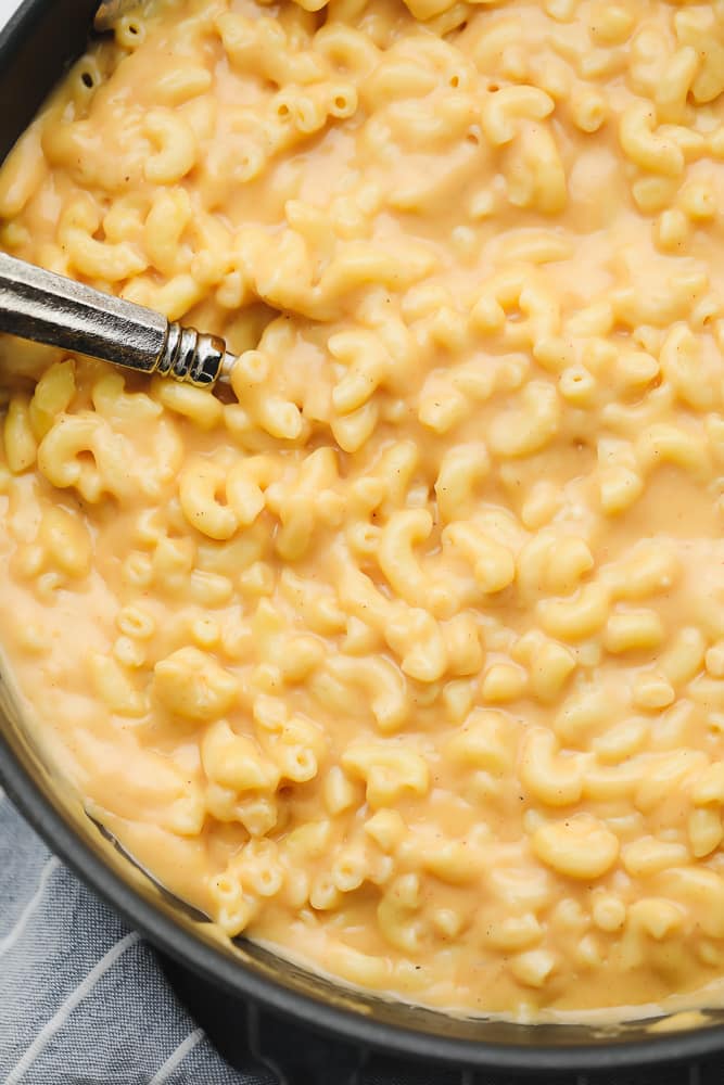 close up on a metal spoon in a pot of saucy mac and cheese