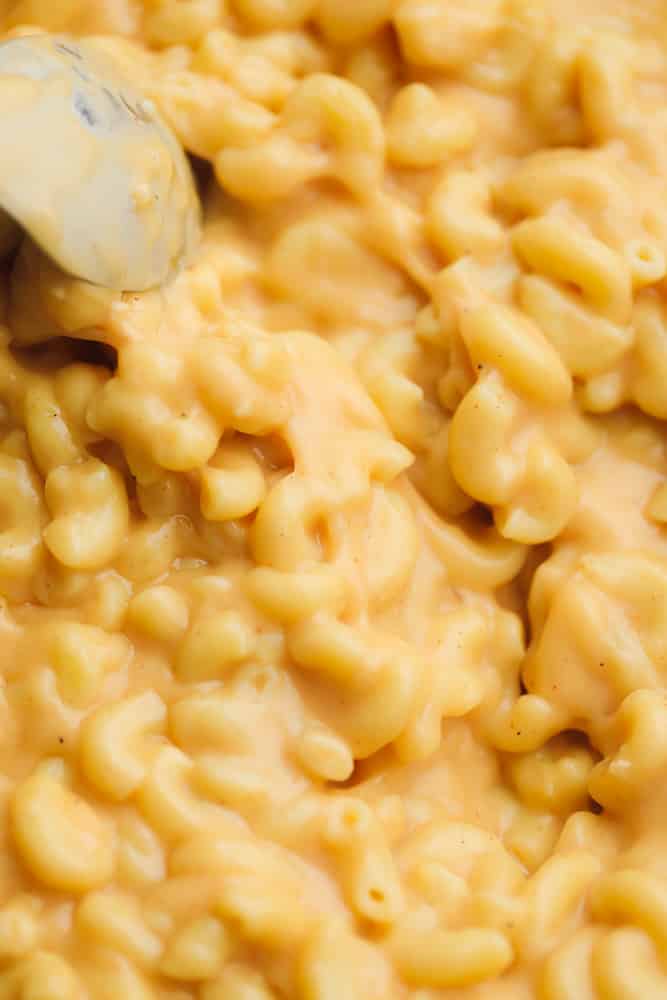 close up on a metal spoon in a pot of saucy mac and cheese