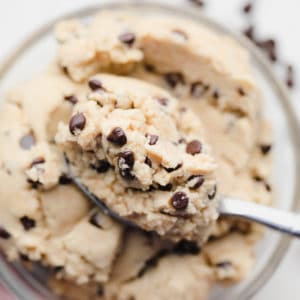 close up on a spoon taking a scoop of chocolate chip cookie dough out of a glass bowl