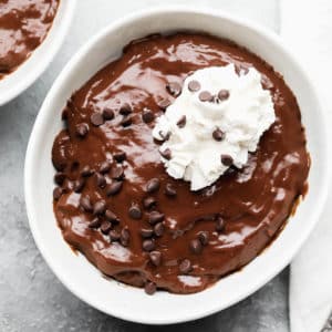 chocolate pudding in a white bowl topped with chocolate chips and whipped cream