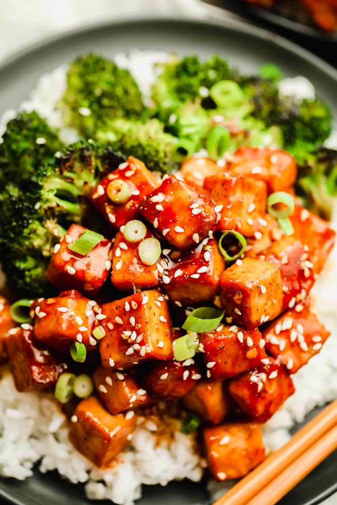close up on brown saucy tofu on a plate with white rice and broccoli