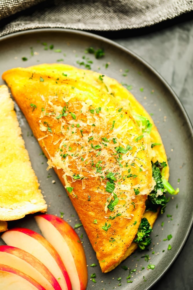 cooked omelette next to fruit and bread on a grey plate