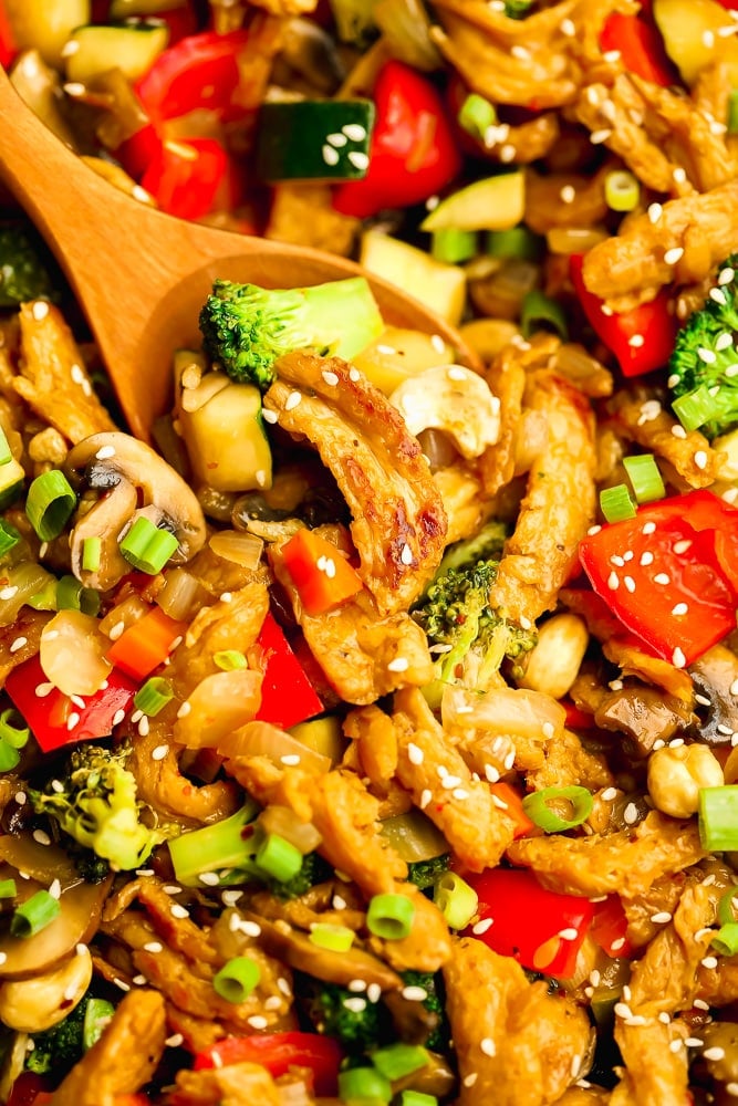 close up on a wooden spoon scooping vegetables and soy curls from a stir fry