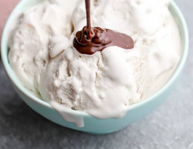 hot fudge being drizzled on vanilla ice cream in a teal bowl