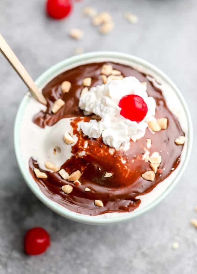 teal bowl of ice cream with vegan hot fudge, whipped cream and a cherry