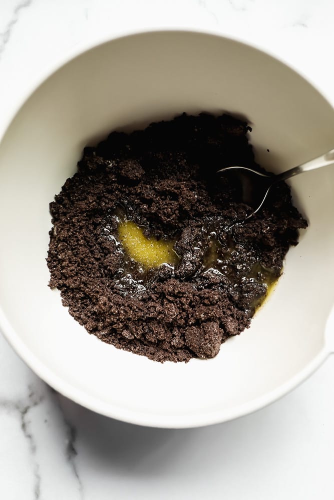 stirring crumbled dark brown cookies and melted butter in a white bowl