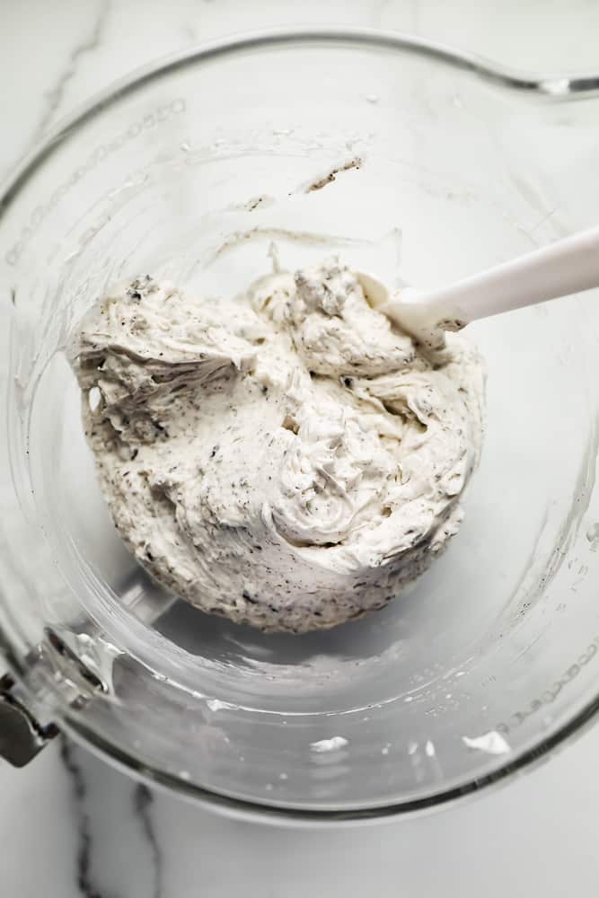 stirring a cookies and cream mixture in a glass bowl with a white spatula.