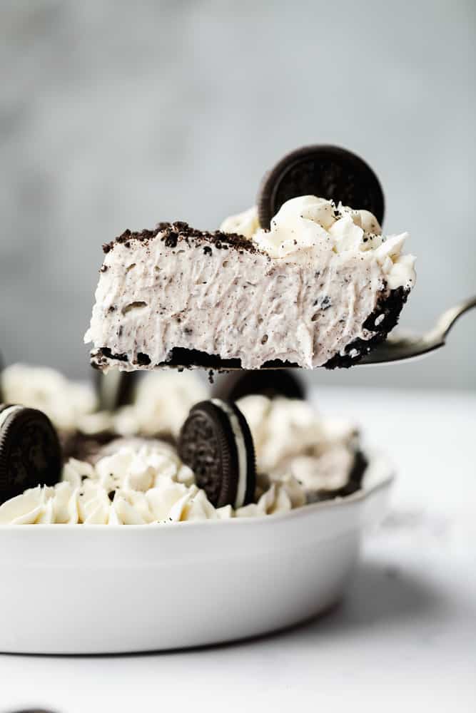 lifting a slice of oreo cheesecake out of a white pie pan.