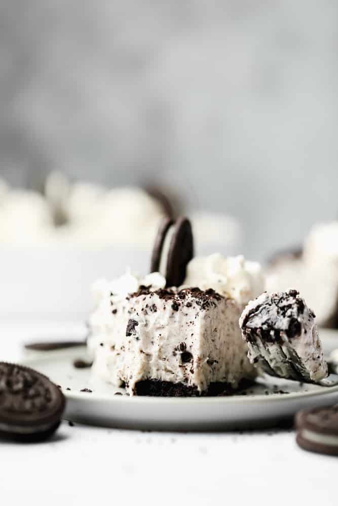 fork taking a bite from a slice of a vegan oreo cheesecake on a white plate