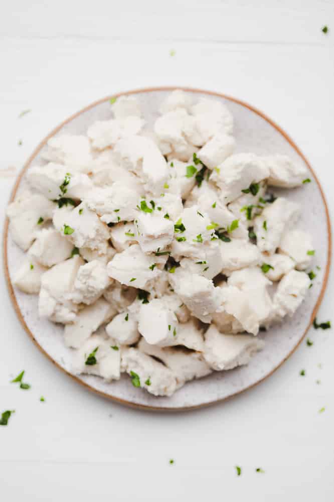 crumbled white cubes of vegan feta cheese topped with green herbs on a white plate