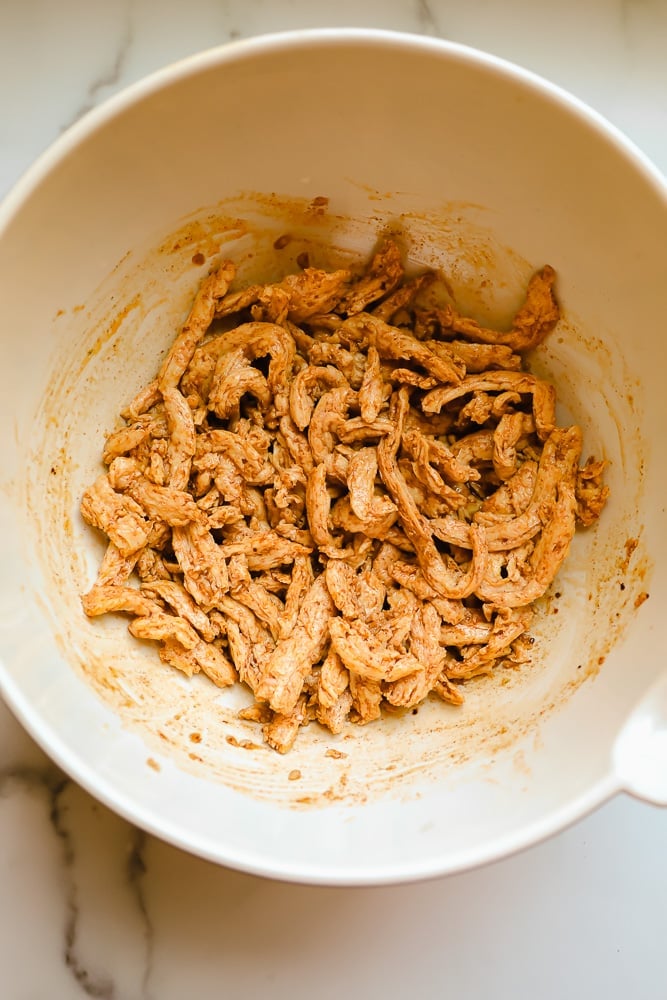 mixing rehydrated soy curls in a white bowl with orange seasonings.
