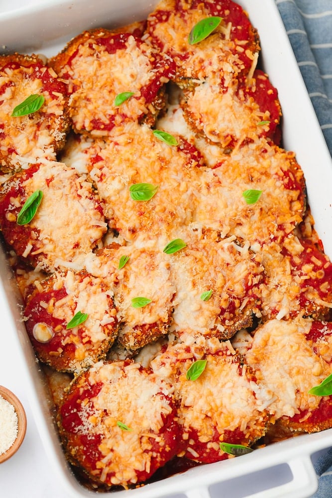 baked eggplant slices with red sauce and melted cheese on top in a white baking dish.