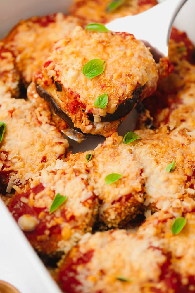 spatula scooping a slice of eggplant parmesan out of a baking dish.