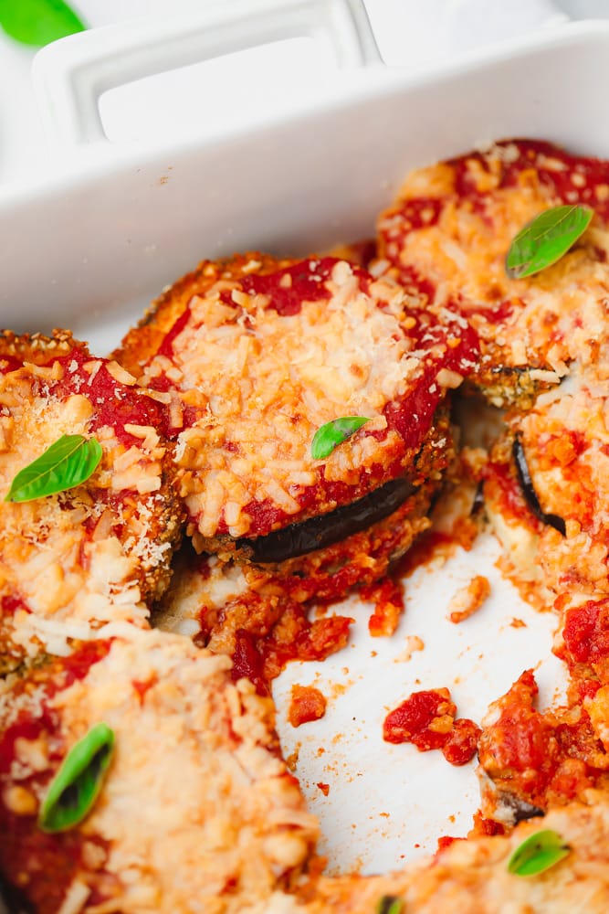 baked eggplant slices with tomato sauce and melted cheese on top in a white baking dish.