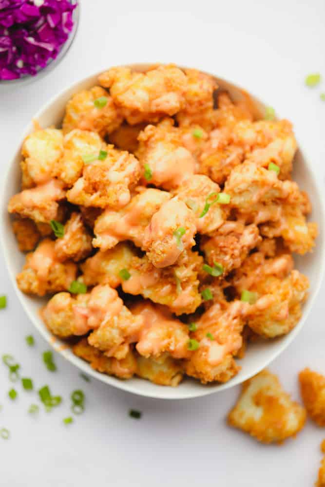 a white bowl filled with fried breaded cauliflower wings with creamy sauce on top