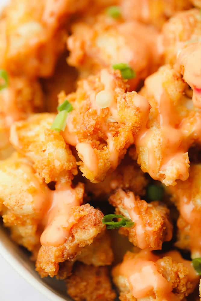 close up on fried cauliflower florets with green herbs and creamy orange sauce on top.