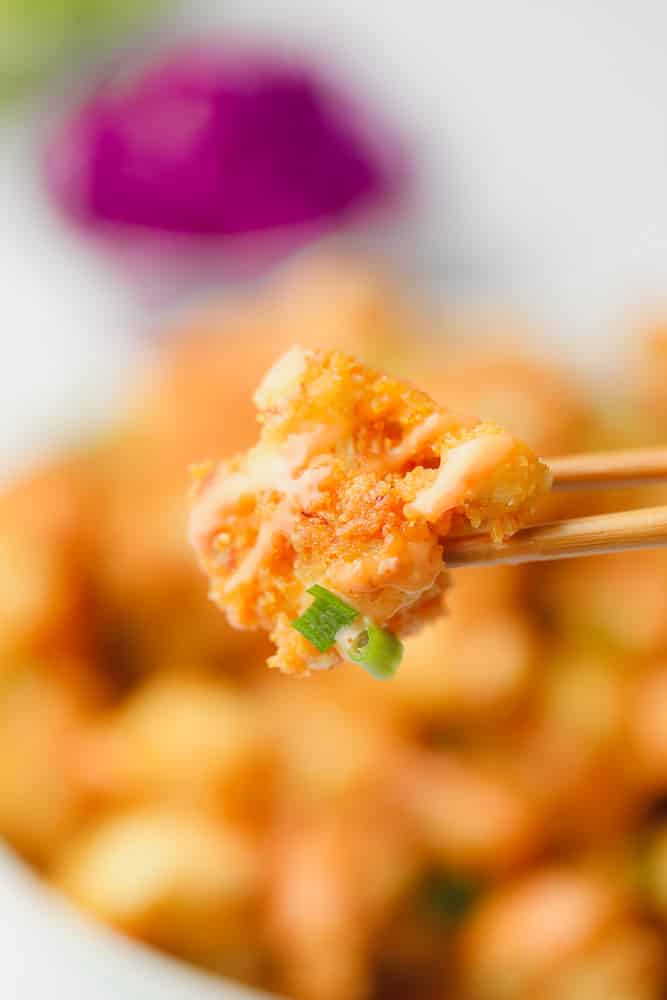 chopsticks holding a piece of fried cauliflower with orange creamy sauce