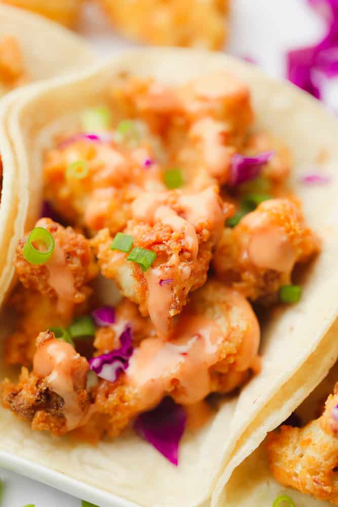 close up on fried cauliflower with orange sauce, purple cabbage, and green herbs in a flour tortilla