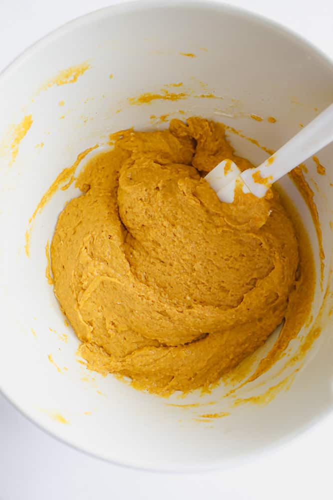 white spatula mixing an orange batter in a white bowl.