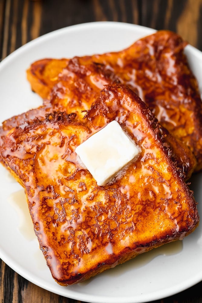 2 slices of vegan pumpkin french toast on a white plate topped with a square of butter.