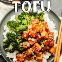 pinterest image of brown saucy tofu on a plate with white rice and broccoli