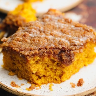 close up on a square slice of orange pumpkin coffee cake on a white plate.