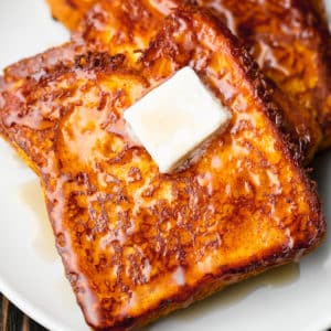 close up on a slice of vegan pumpkin french toast on a white plate topped with a square of butter.