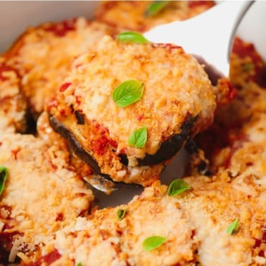 spatula scooping a slice of eggplant parmesan out of a baking dish.