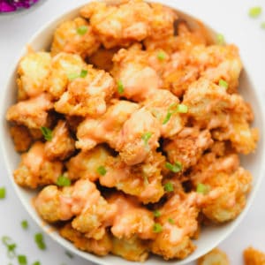 a white bowl filled with fried breaded cauliflower wings with creamy sauce on top