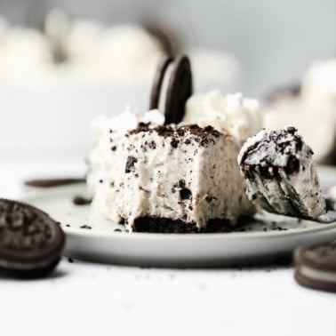 fork taking a bite from a slice of a vegan oreo cheesecake on a white plate