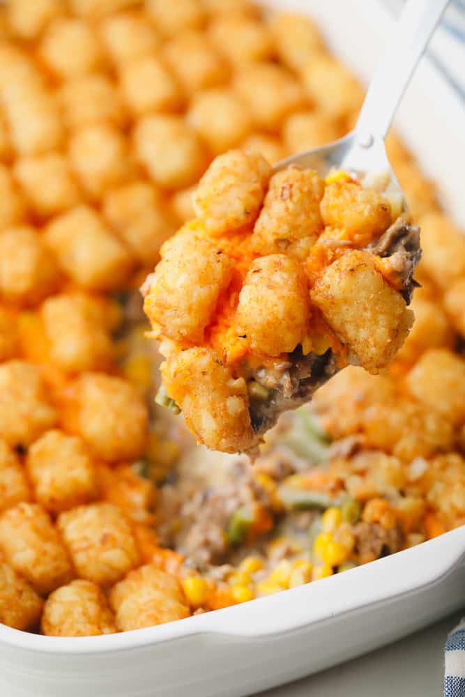 close up on a metal spoon holding a scoop of a baked tater tot casserole.