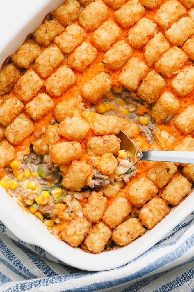 metal spoon scooping some baked tater tot casserole out of a white casserole dish.