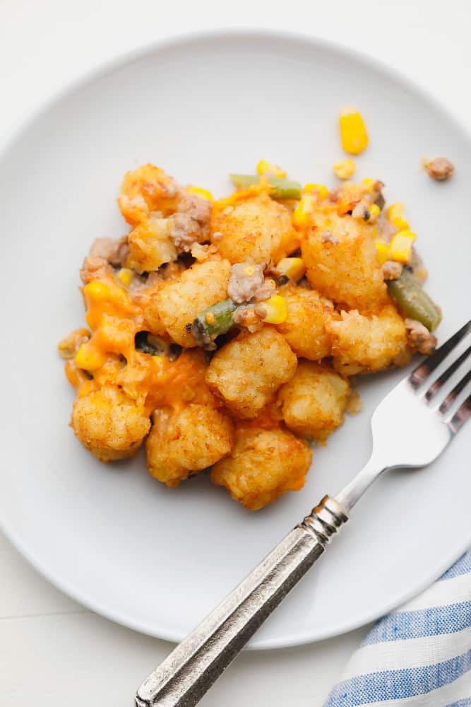 scoop of baked tater tots, corn, and green beans on a white plate next to a fork.