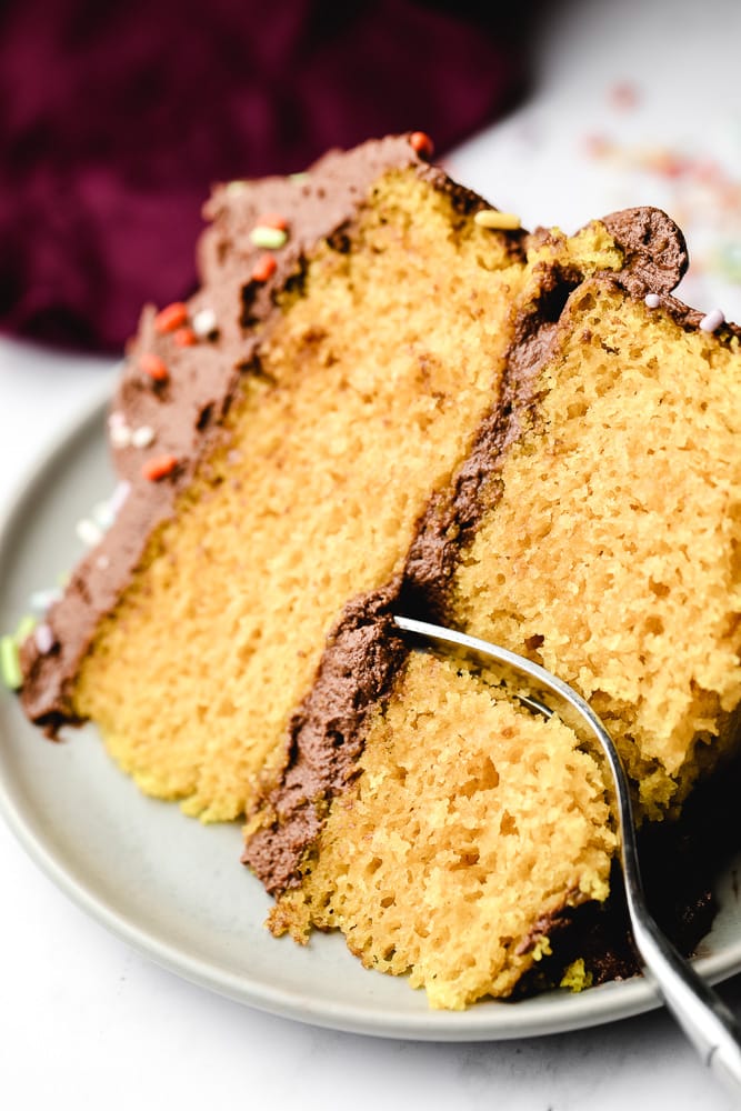 Fork taking a bite out of a piece of yellow cake on a white plate.