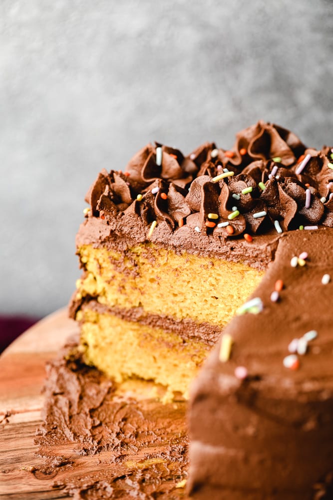 yellow cake with chocolate frosting with slices missing on a wood board.