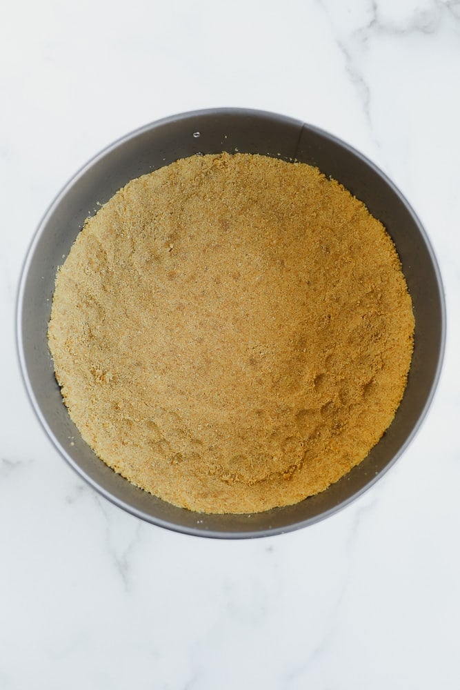 golden brown graham cracker crust on the bottom of a round metal pan.