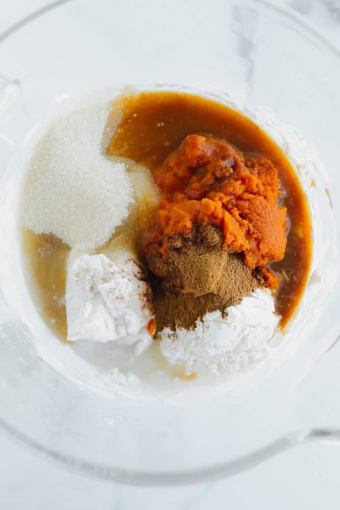 pumpkin puree, sugar, coconut cream, liquid, and spices in a pile in a glass bowl.